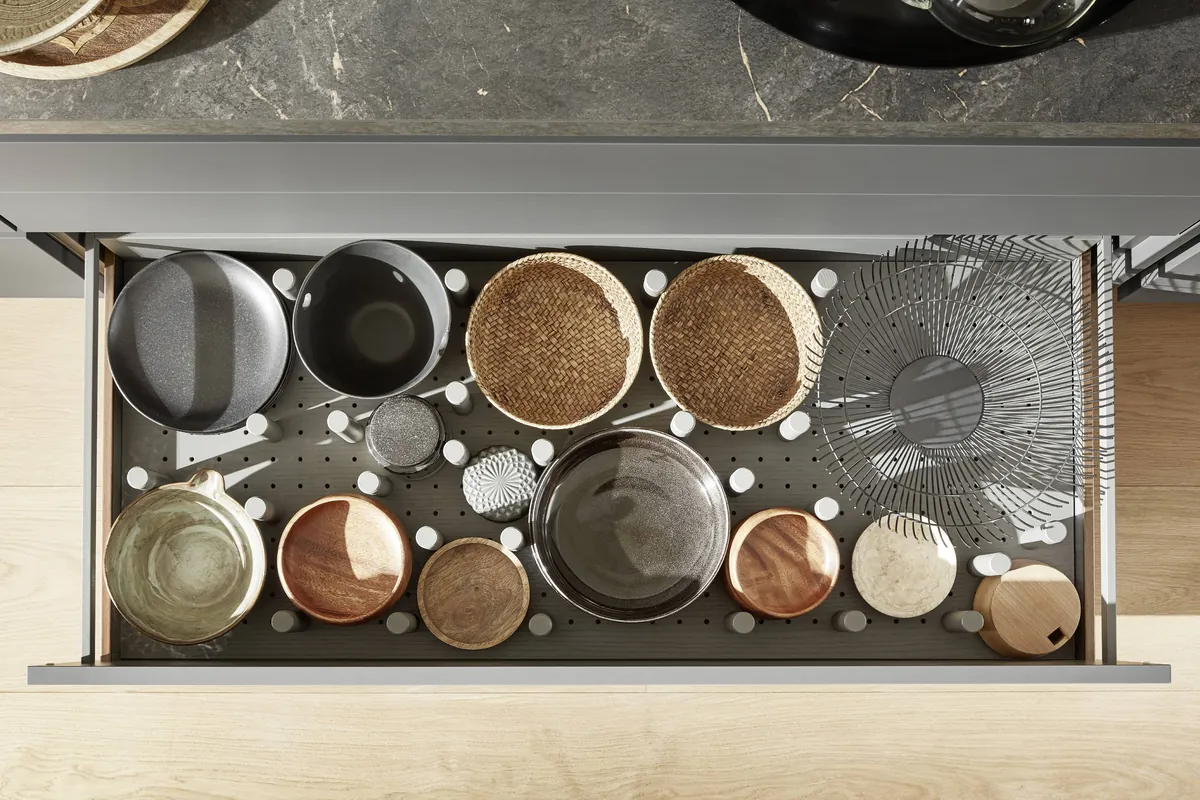 A drawer seen from above, fitted with pegs holding pots, bowls and baskets