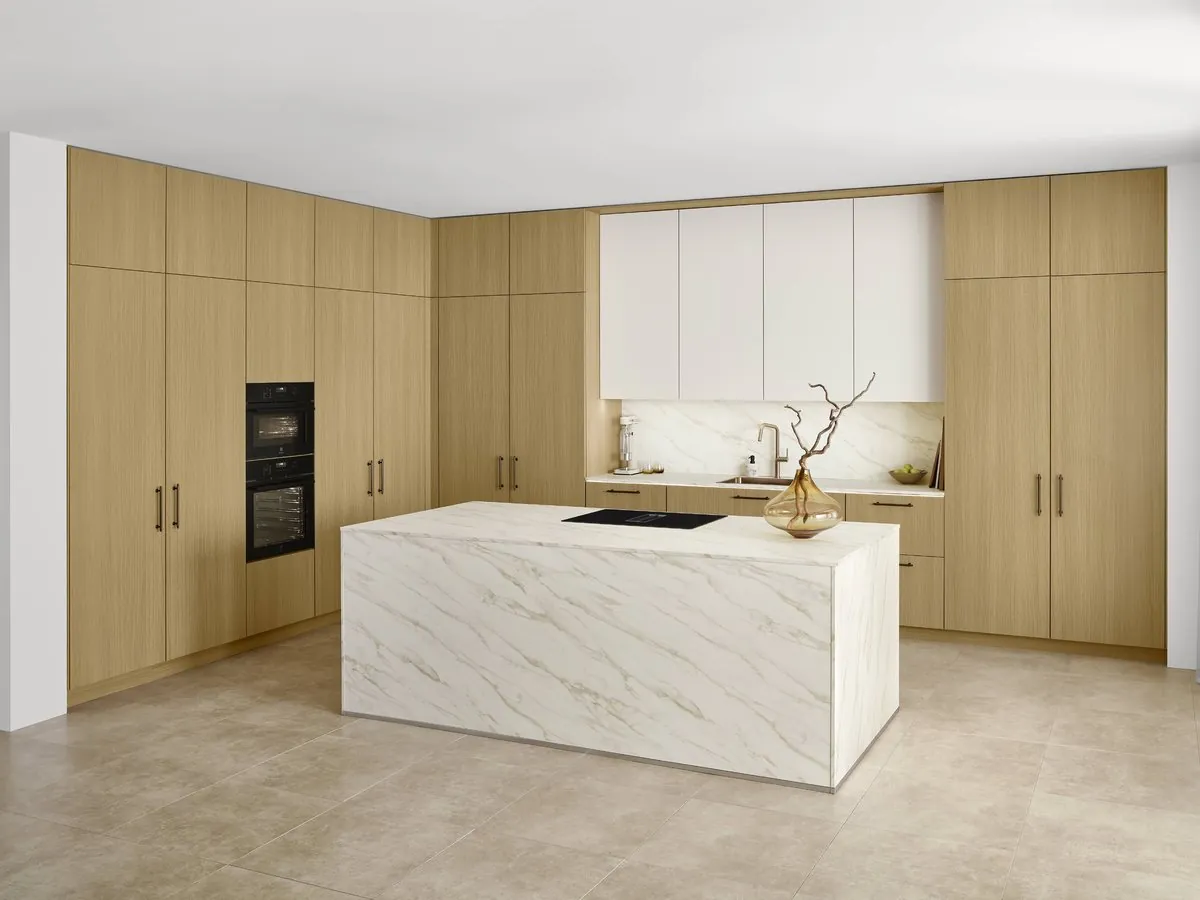 A kitchen in pale oak tall units around a marble-effect island