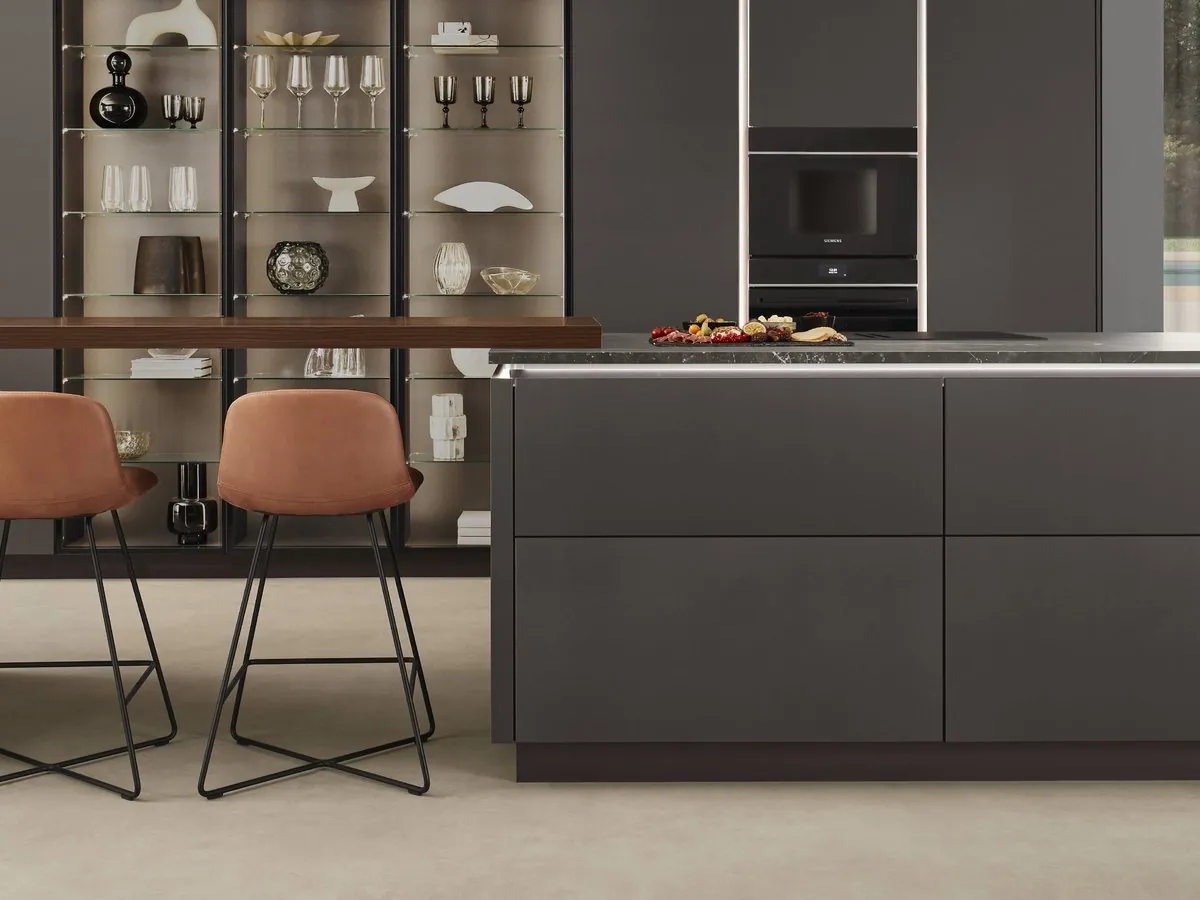 A dark kitchen with a lit glass display unit and an island with a timber breakfast bar