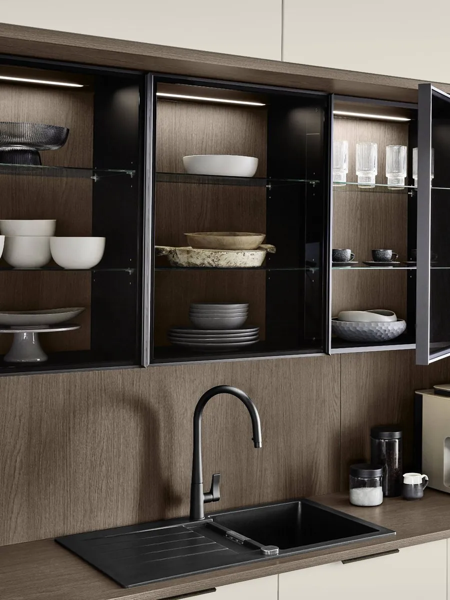 Lit glass wall units above a walnut splashback and a black sink