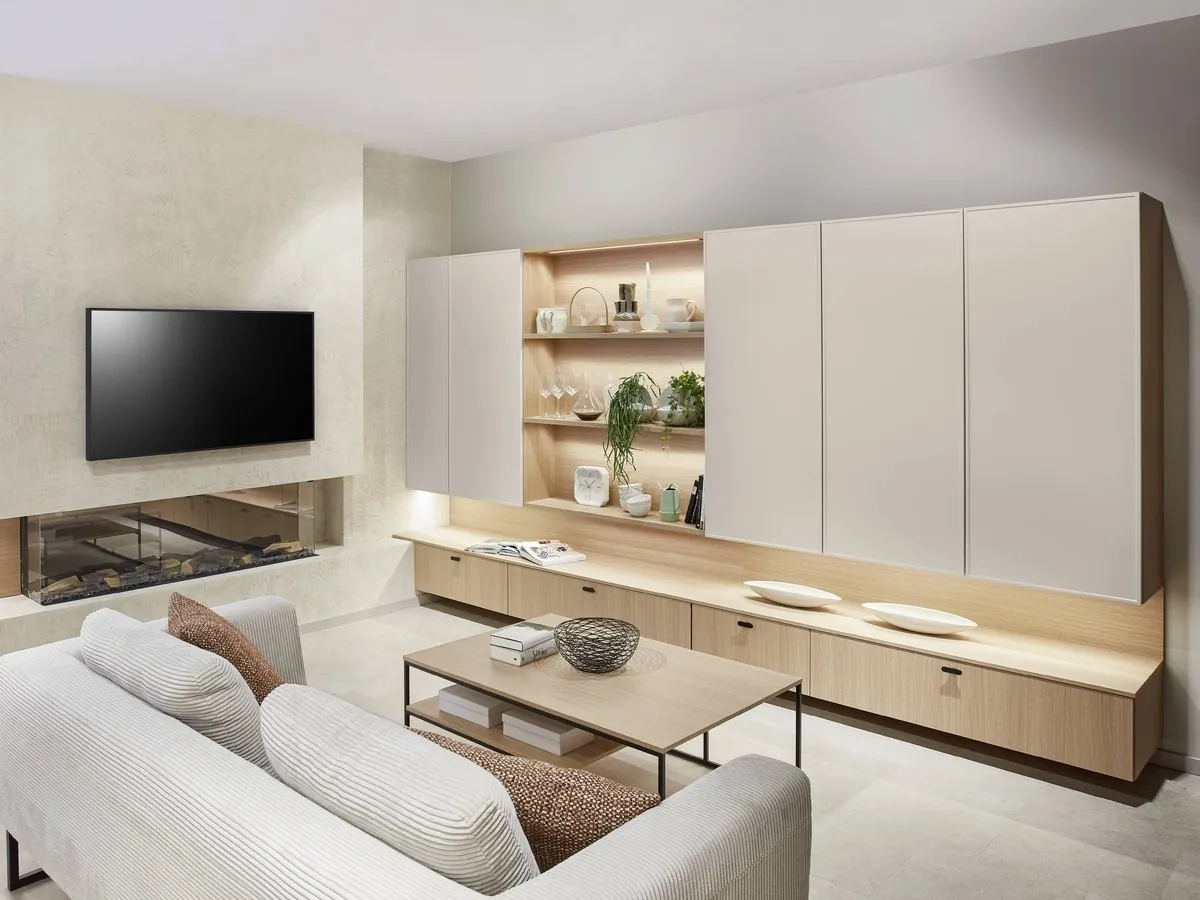 A living room wall of pale cabinetry and lit timber shelving around a fireplace and screen