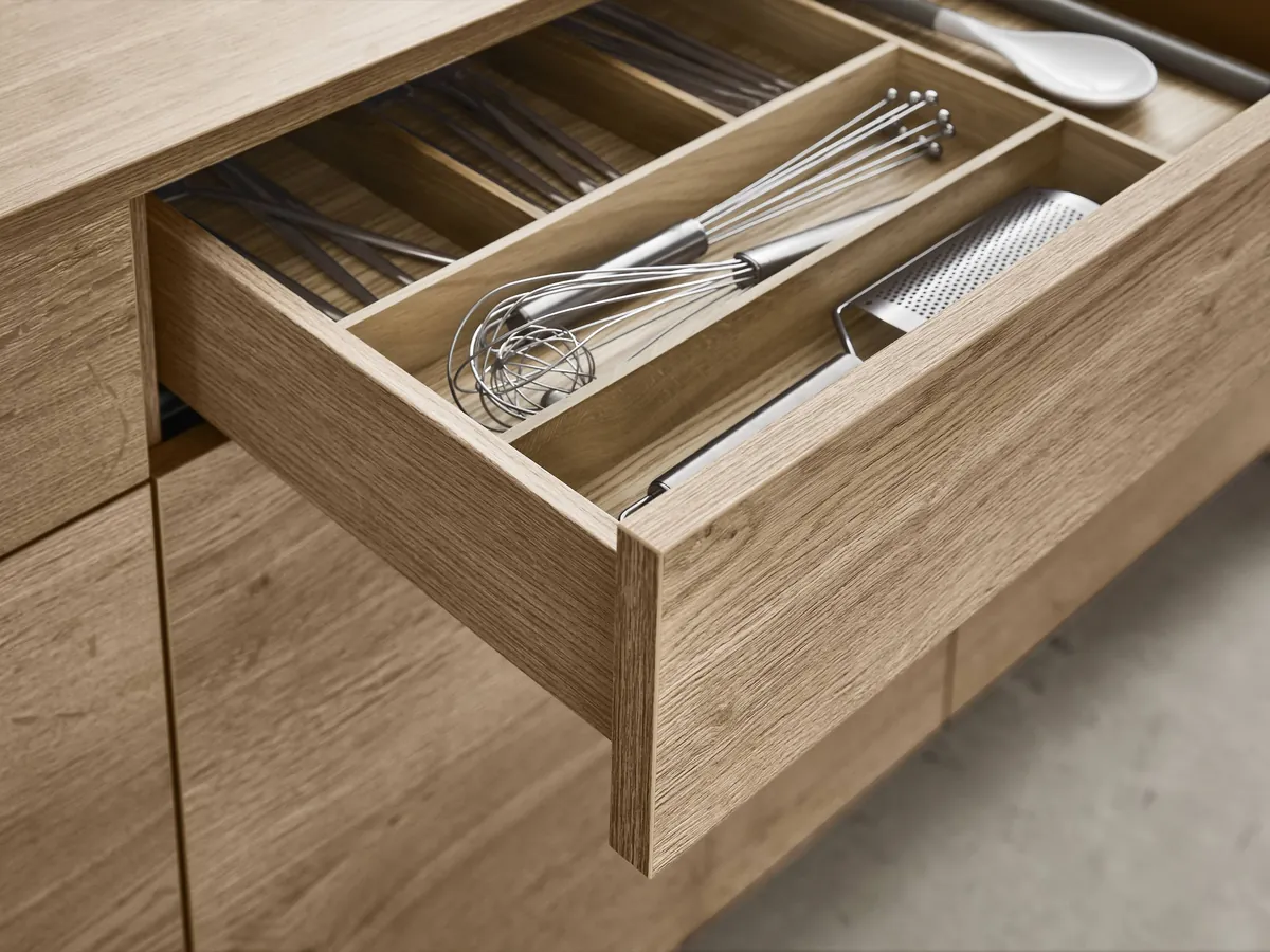 An oak-grain drawer fitted with a timber insert for cutlery and utensils