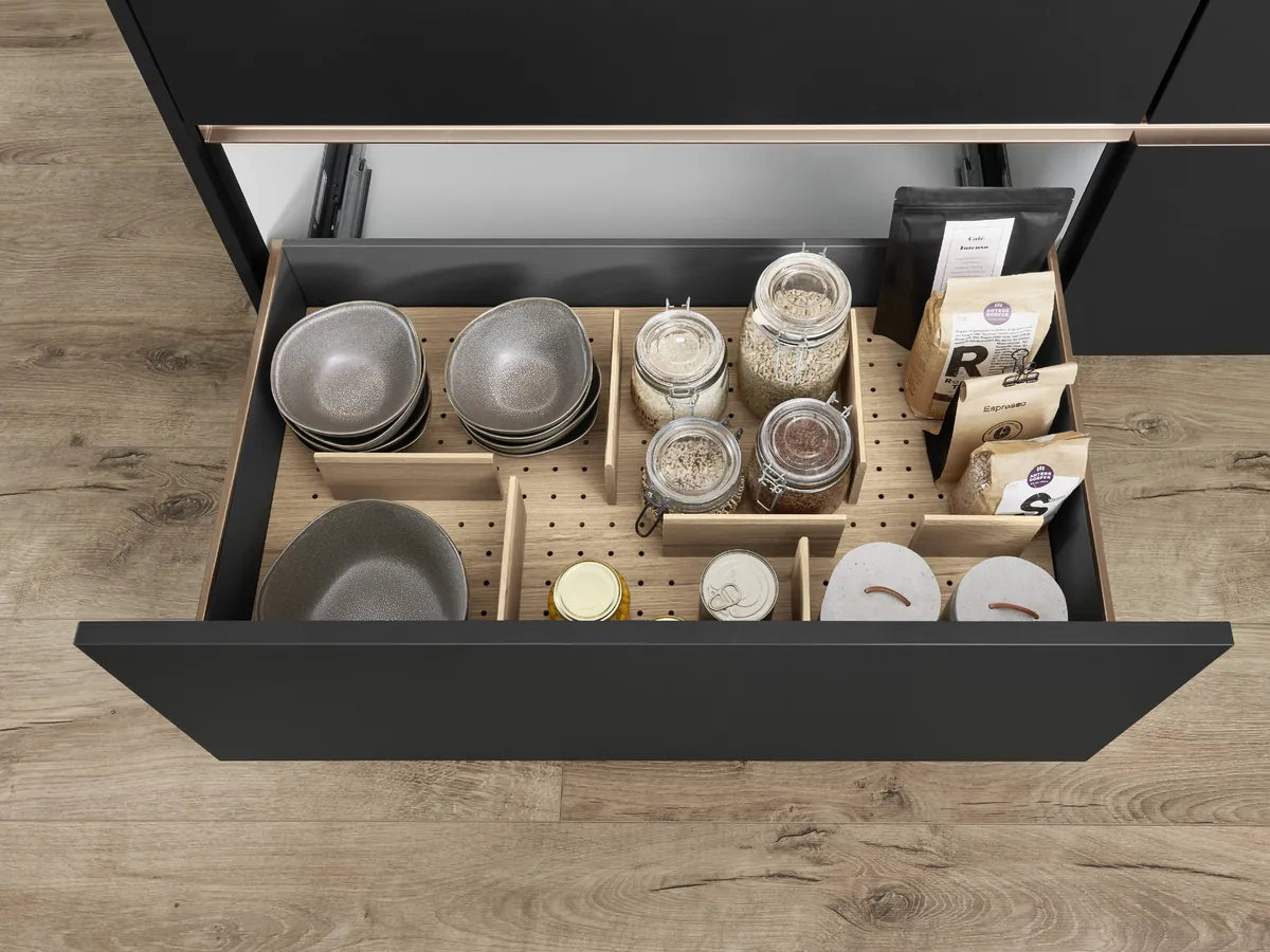 A wide drawer seen from above, with pegs holding bowls, jars and spices