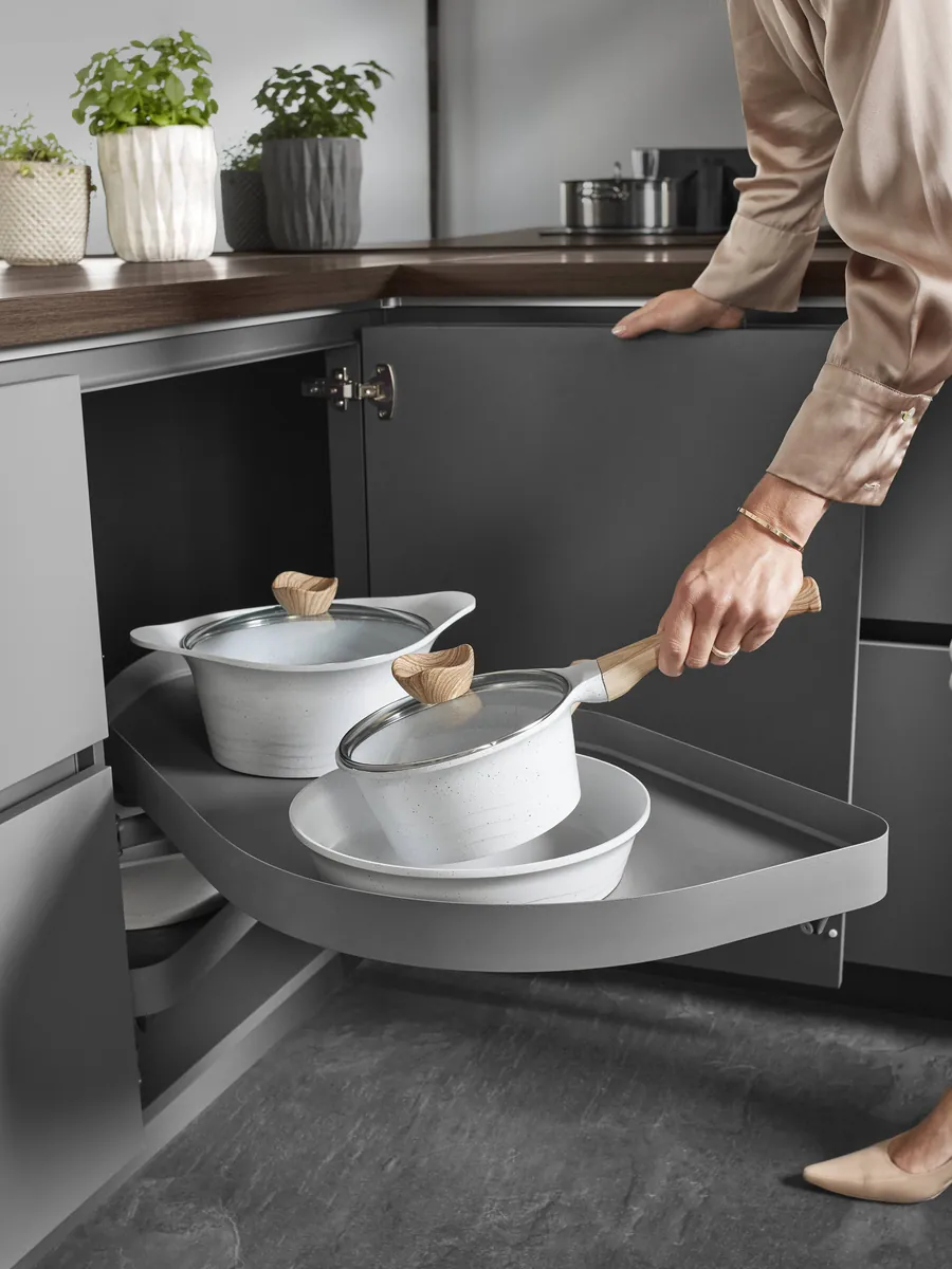 A curved corner shelf swung out of a dark cabinet, holding white pans