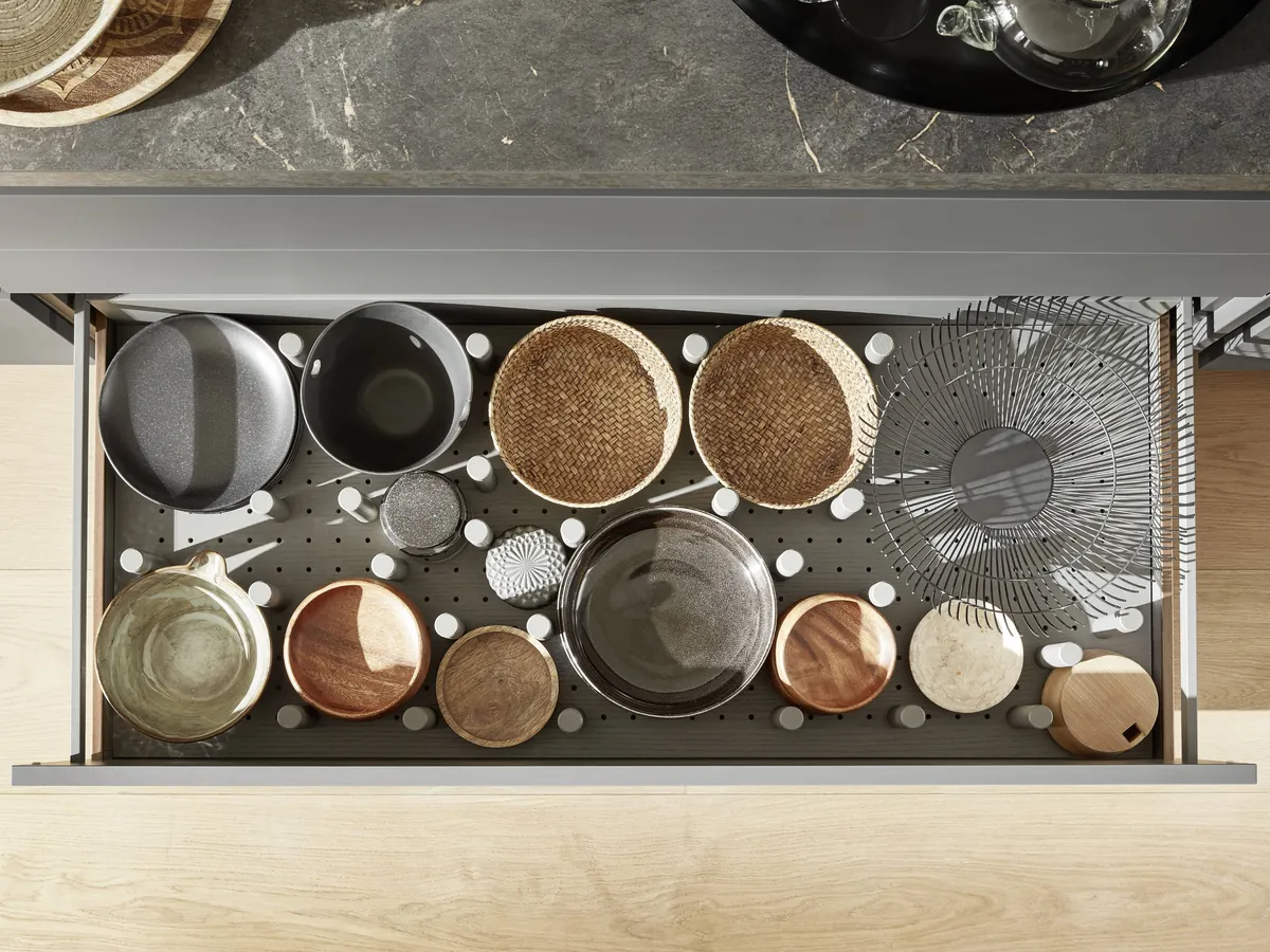 A wide drawer seen from above, with pegs holding pans, bowls and baskets in place
