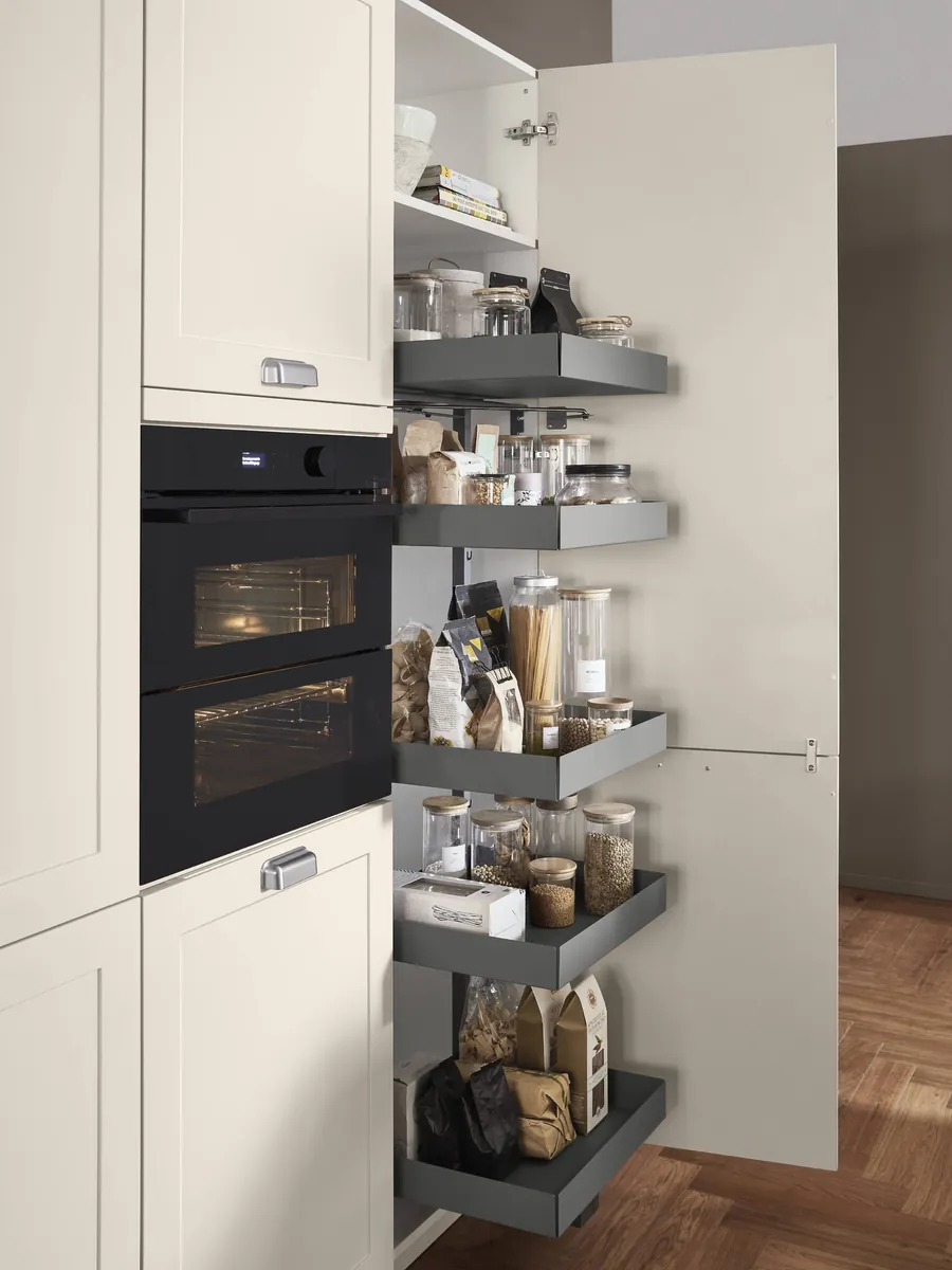 A tall larder open beside a built-in oven, its shelves swung out with the door