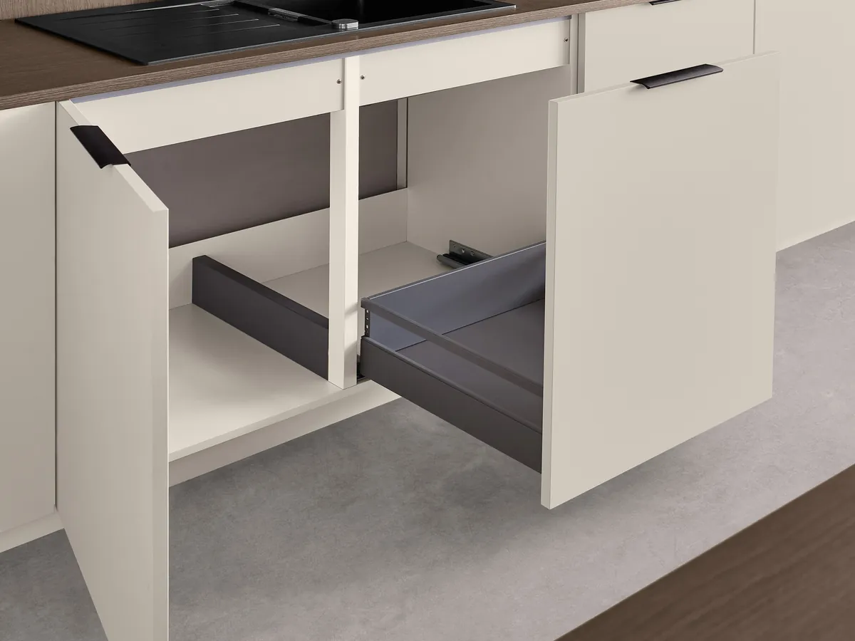 A sink cabinet open on a drawer shaped around the plumbing